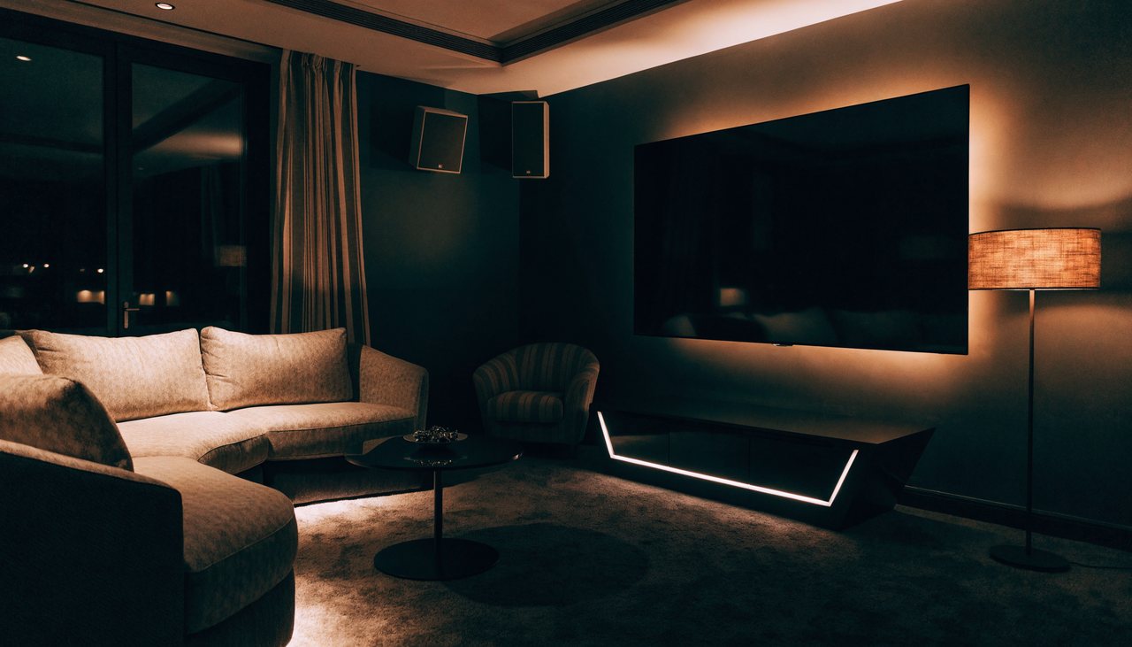 A home media lounge with a large wall-mounted TV, ambient backlight and multi-room audio