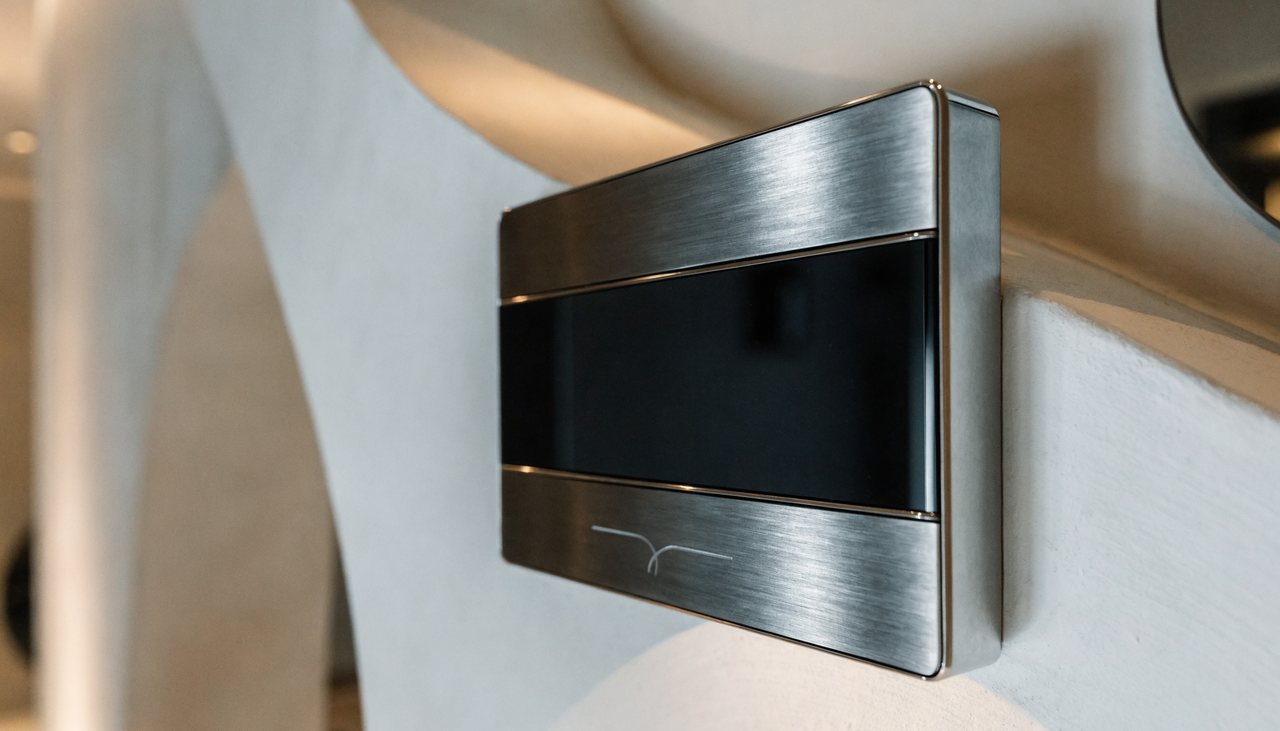 A premium brushed-metal and glass KNX smart keypad on a designer wall